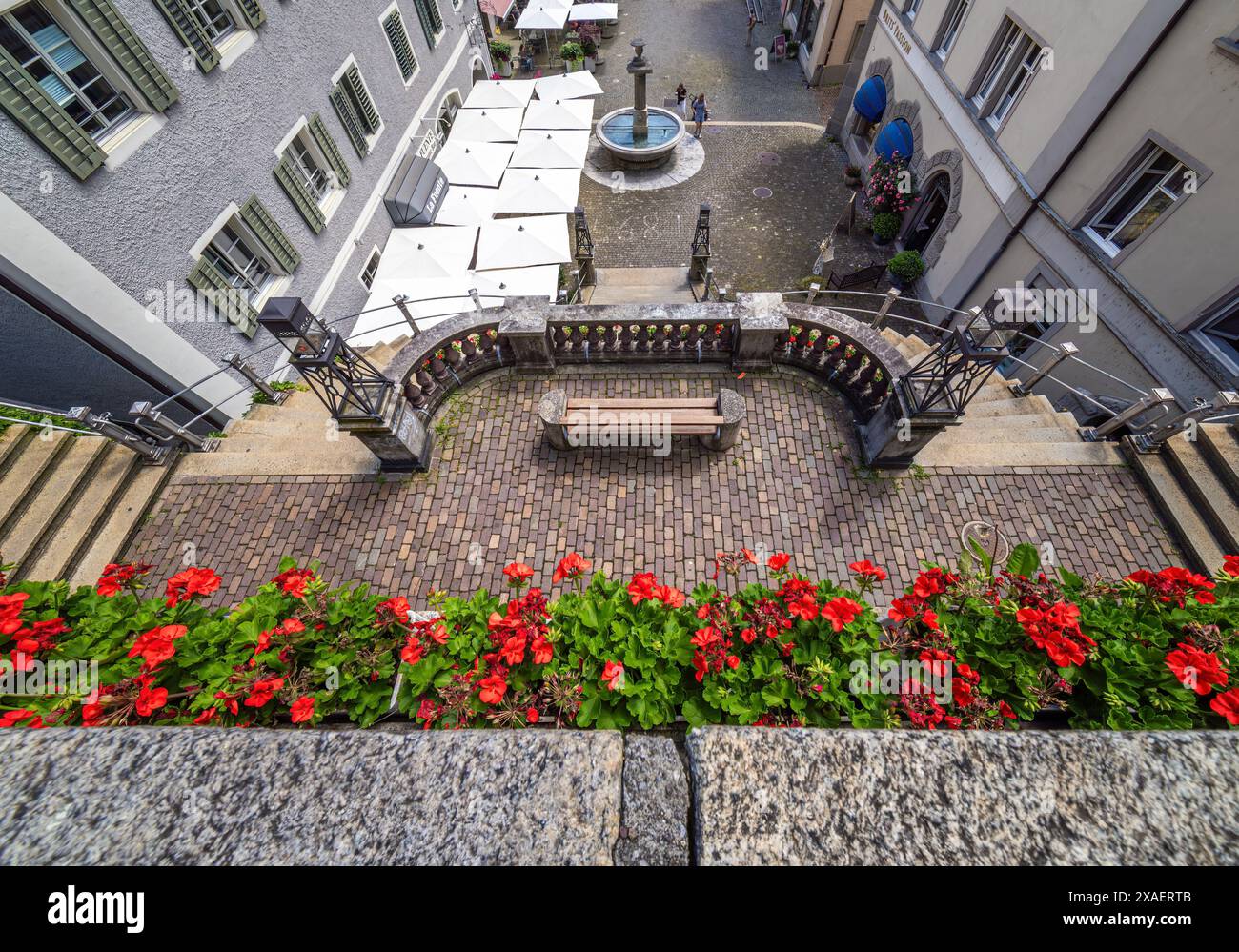Rapperswil, Schweiz - 5. Juni 2024: Malerischer Innenhof in Rapperswil mit roten Blumen, Holzbank, Steinbrunnen, Kopfsteinpflaster. Stockfoto