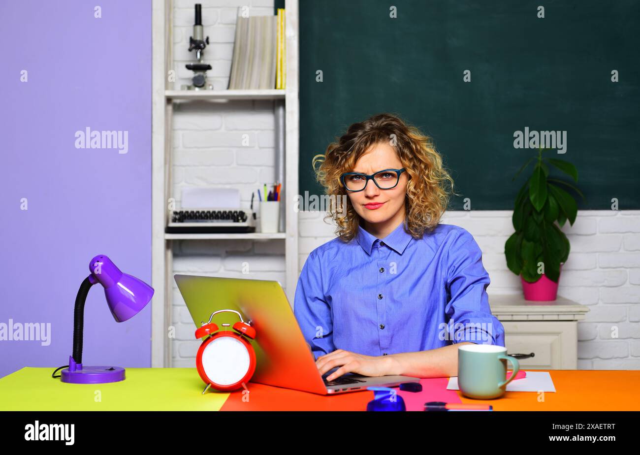Lehrerjob. Die runzelnde Lehrerin arbeitet mit dem Laptop im Klassenzimmer. Konzentrierter Schüler in Brille, der Webinar auf Laptop ansieht und sich auf vorbereitet Stockfoto