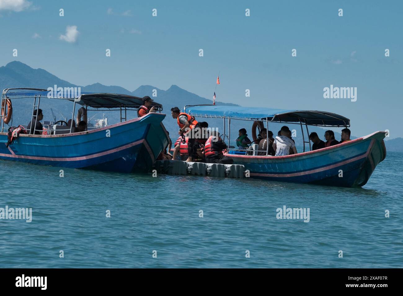 Zwei Boote sind im Wasser mit Menschen auf ihnen. Eines der Boote ist blau und das andere rot Stockfoto