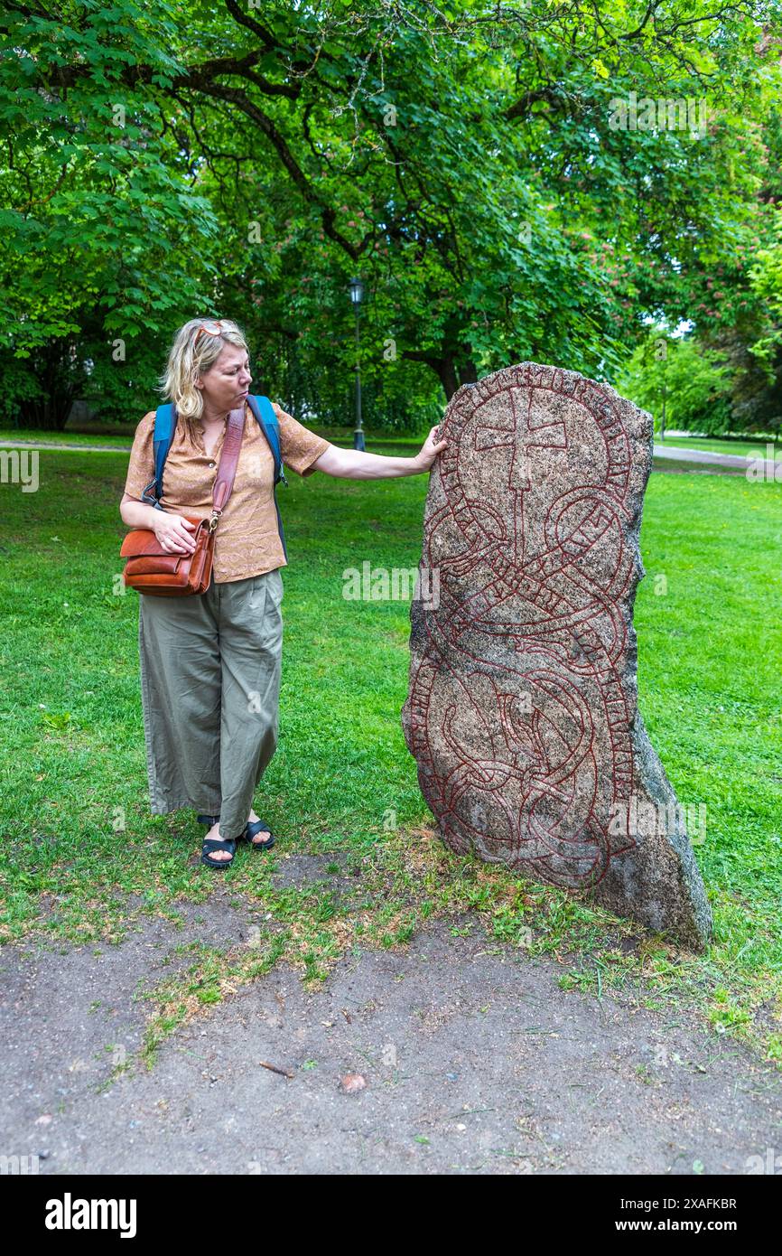 Runensteine im Uppsala University Park. Die Stadtführerin Katja Jahn erklärt, dass Runensteine zum Gedenken an die Familie von jemandem errichtet wurden. Die Inschrift enthält den Namen und die Urkunden des Verstorbenen sowie den Namen des Auftraggebers und des Handwerkers, der den Stein geschnitzt hat. Uppsala, Schweden Stockfoto