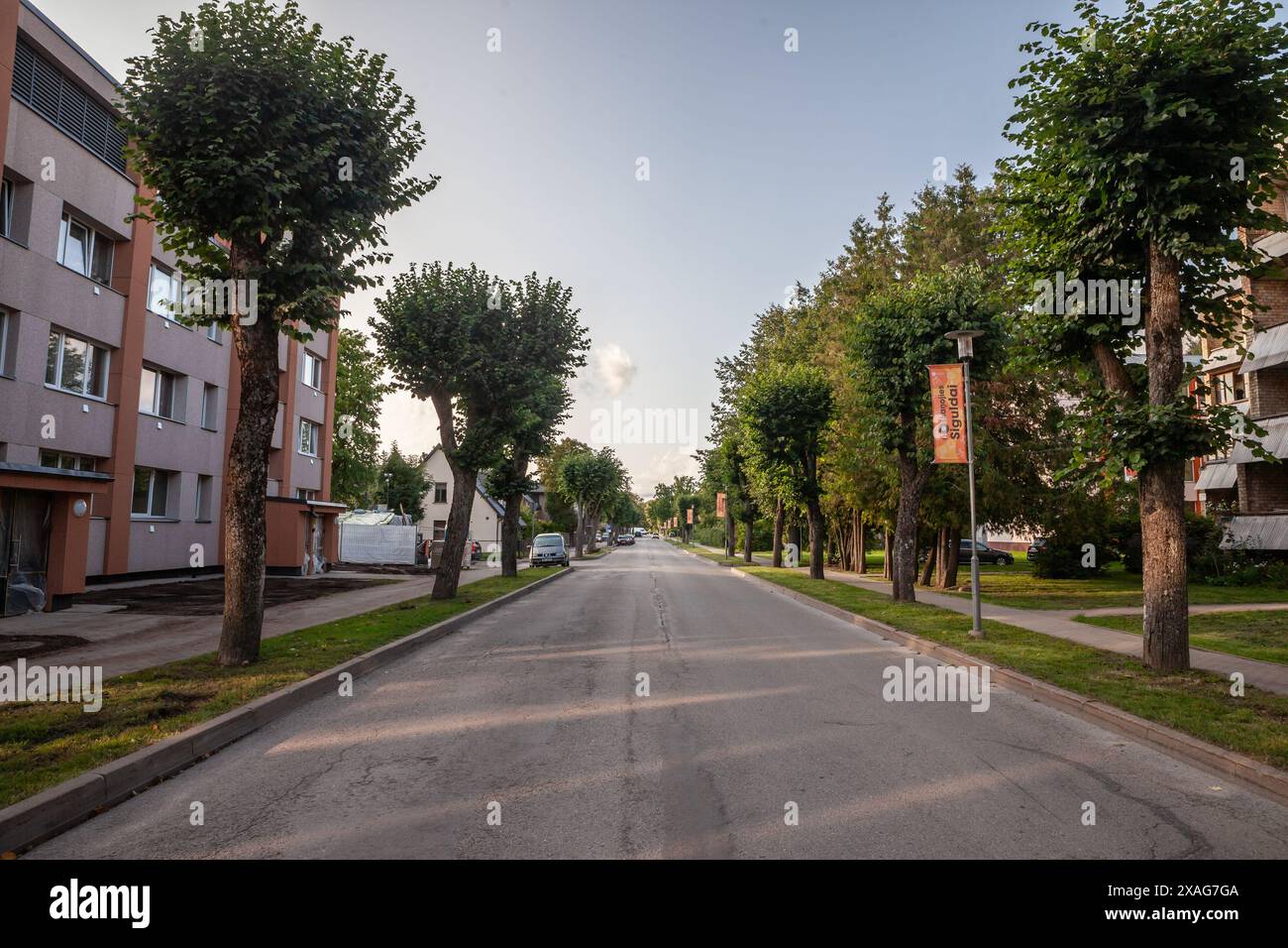Bild einer Wohnstraße in der Abenddämmerung in Sigulda, Lettland, mit Autos, die an Gemeinschaftsgebäuden geparkt sind. Stockfoto