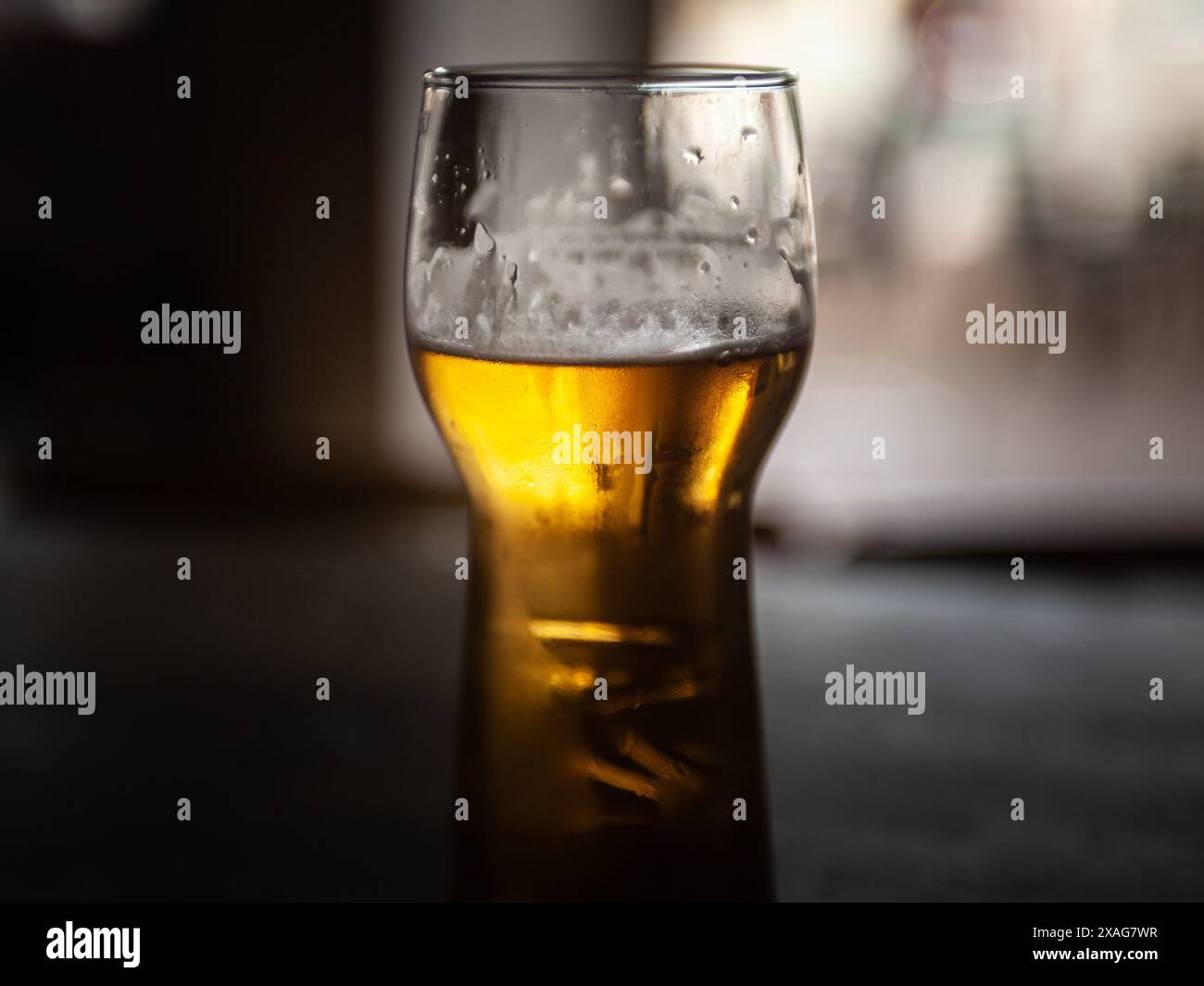 Dieses Bild zeigt eine Nahaufnahme eines gekühlten Glases Bier, das seinen goldenen Farbton und seinen schäumenden Kopf zeigt. Das Bier, ob ein Bier oder ein Bier, verströmt Stockfoto