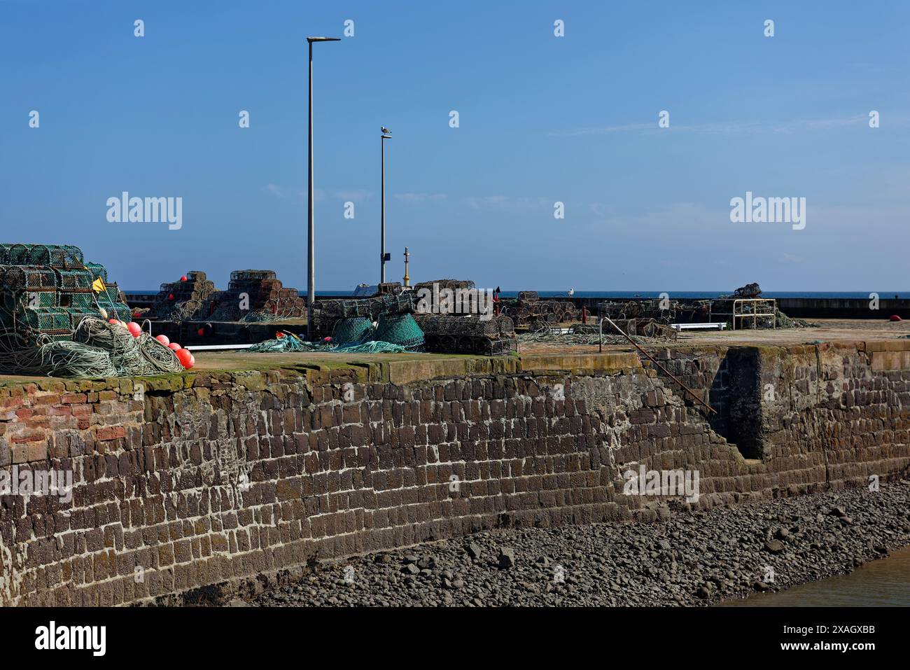 Versteckte Steintreppen zum Wasser bei Ebbe am Arbroath Harbour, mit Angelausrüstung und Töpfen, die am Kai verstreut sind. Stockfoto