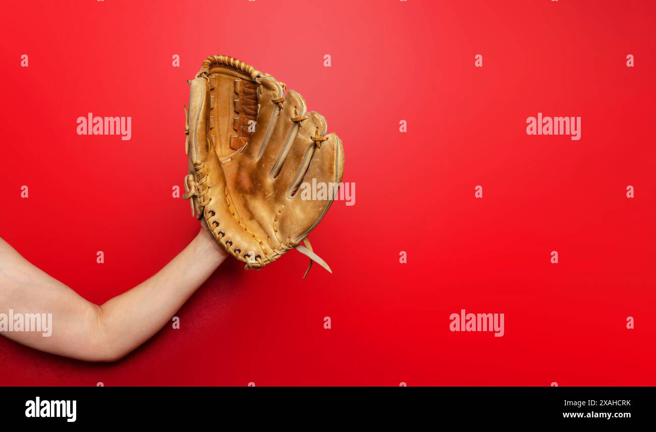 Baseballhandschuh auf der Hand der Frau. Roter Hintergrund, Kopierraum. Aktiver Sport, Meisterschaft, Sieg Stockfoto