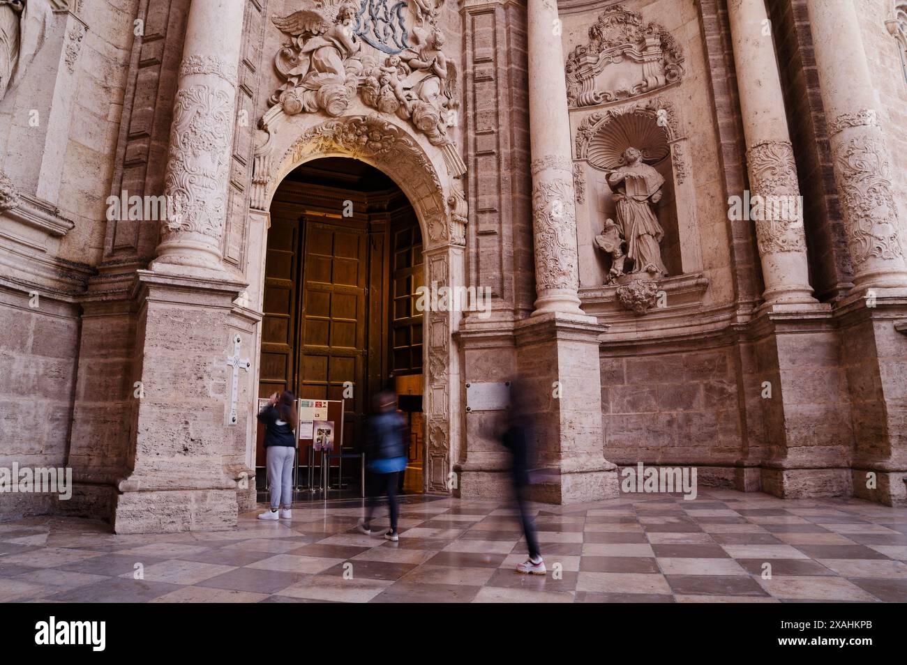 Die Besucher gehen am kunstvollen Eingang der Kathedrale von Valencia vorbei, wo sie ihre komplizierten Steinschnitzereien und die historische Architektur bewundern Stockfoto