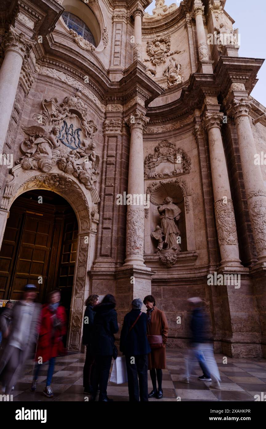 Die Besucher gehen am kunstvollen Eingang der Kathedrale von Valencia vorbei, wo sie ihre komplizierten Steinschnitzereien und die historische Architektur bewundern Stockfoto
