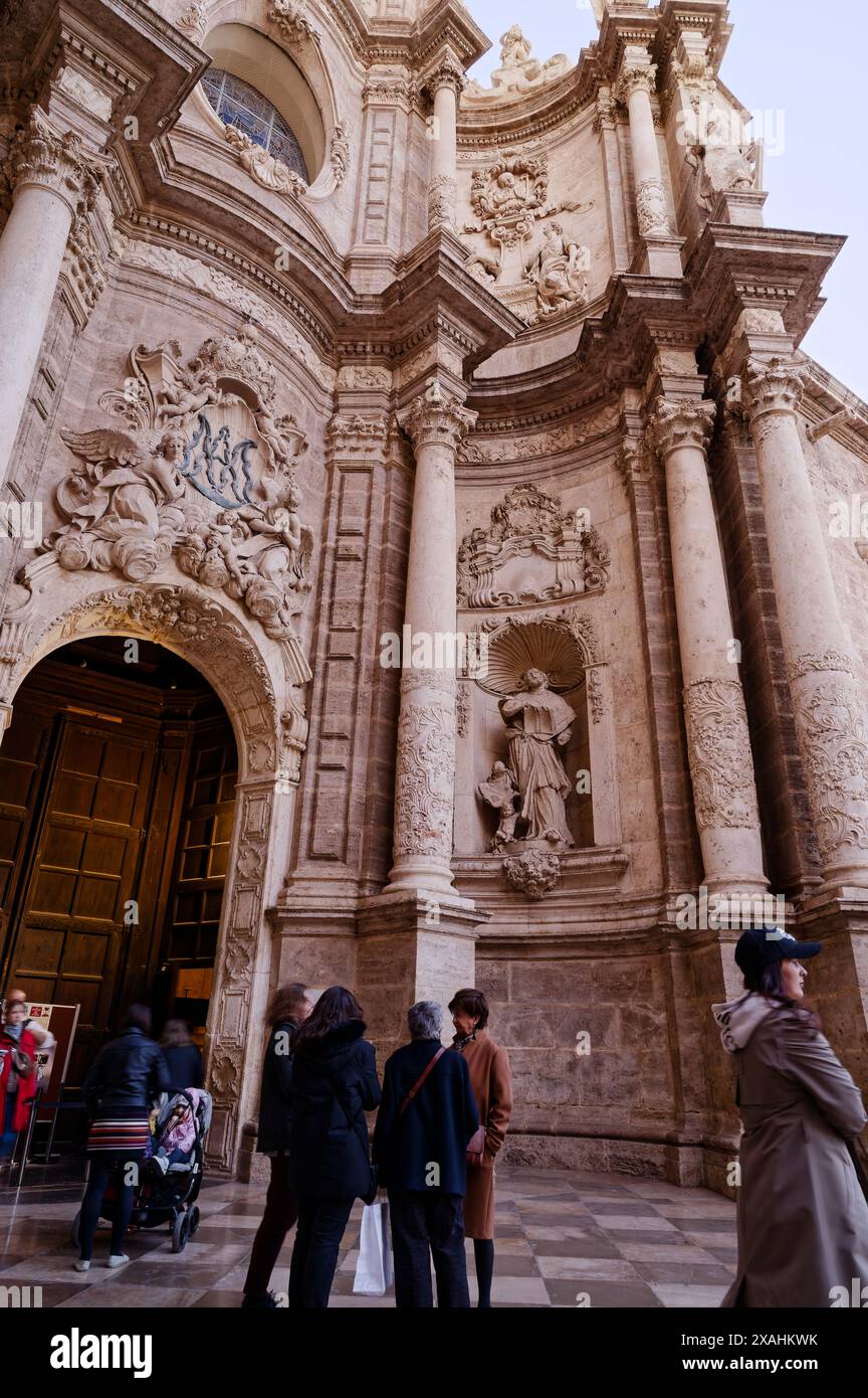 Die Besucher gehen am kunstvollen Eingang der Kathedrale von Valencia vorbei, wo sie ihre komplizierten Steinschnitzereien und die historische Architektur bewundern Stockfoto