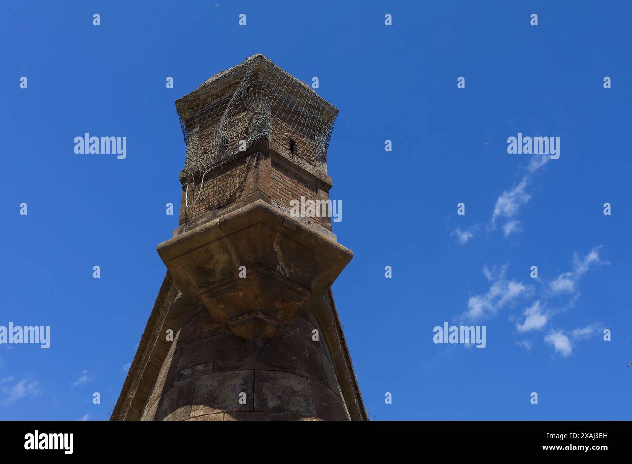 Fotografie eines alten spanischen Schlossturms, bedeckt mit Netz, roter Backsteinwachturm mit hellblauem Himmel darüber Stockfoto