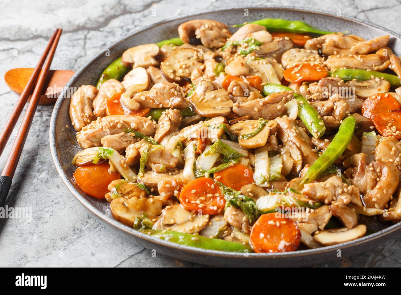 Moo Goo Gai Pan in Scheiben geschnittenes Huhn, Schneeroben, Karotten, Bambussprossen und Pilze in einer dickköpfigen braunen Soße auf dem Teller auf dem Ta gebraten Stockfoto