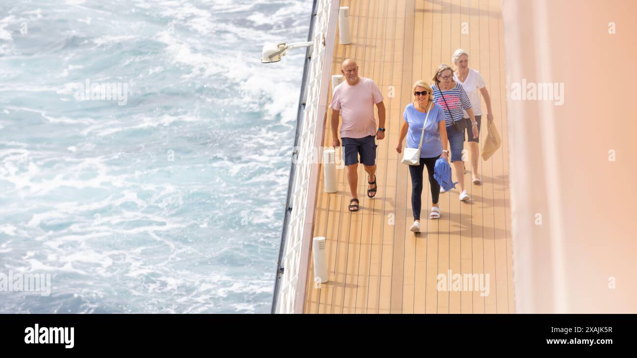 Ältere, reife Kreuzfahrtpassagiere, die einen zügigen Spaziergang in der sauberen Meeresluft rund um ein Promenadendeck machen Stockfoto