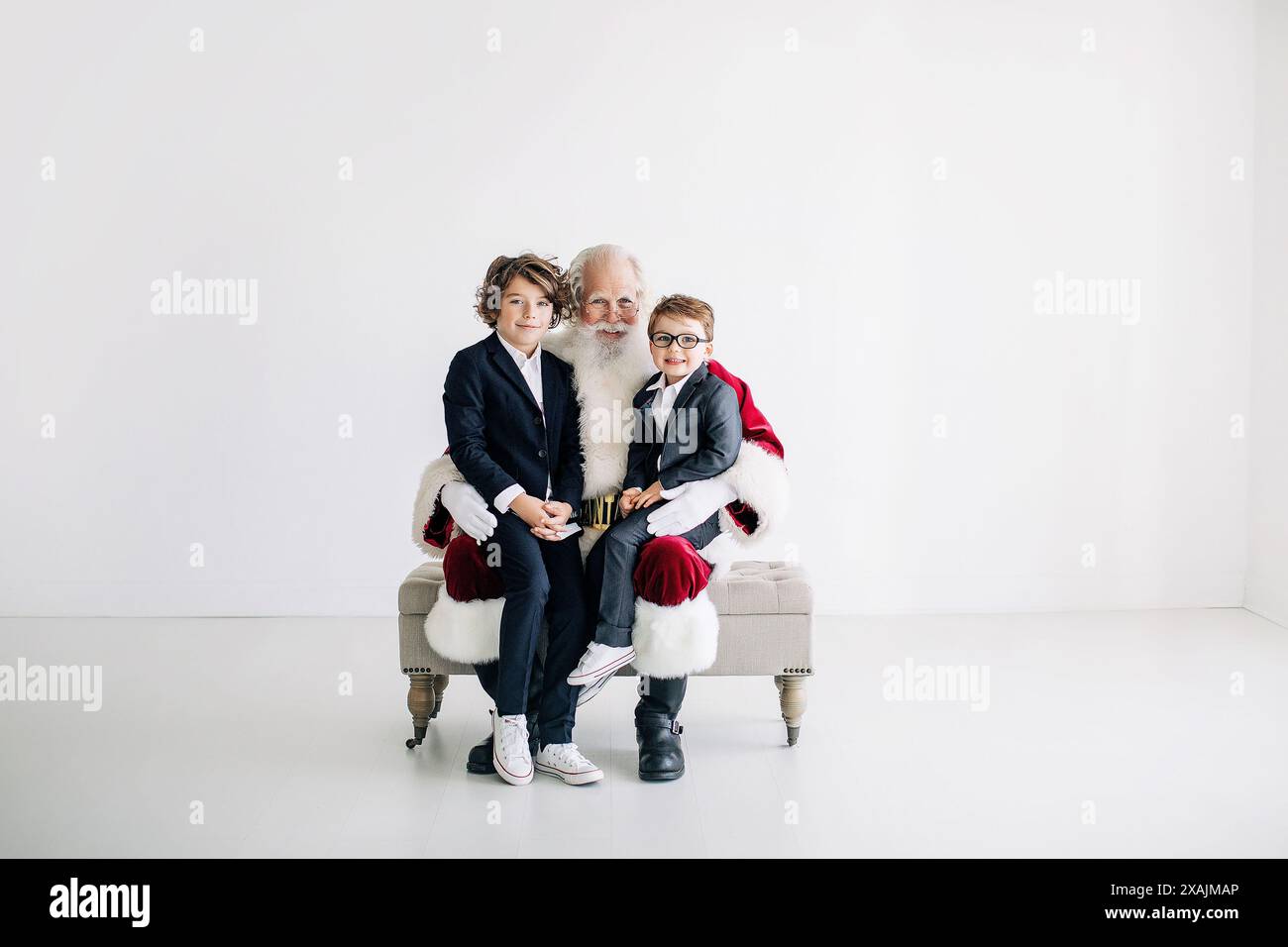 Weihnachtsmann mit zwei Jungs in Anzügen, die auf einer Bank gegen einen Minima sitzen Stockfoto