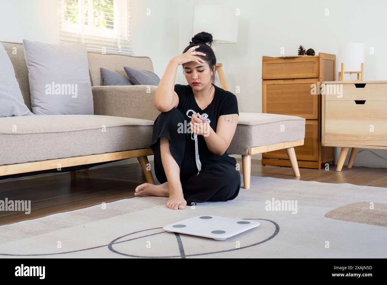 Gestresste Frau, die auf dem Boden sitzt, mit Maßband und Waage. Das Konzept von Gewichtsproblem und Angst Stockfoto