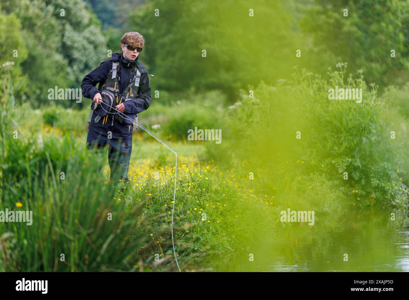 Ein Teenager Fliege, die im Sommer an einem Flussufer in Devon, England, Forellen fischt. Stockfoto