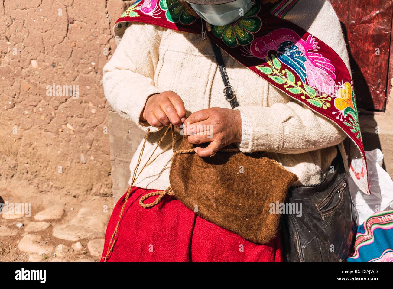 Arme indigene erwachsene Frau Handwerkerin mit blauer Maske und typischer Ahnenweberei in Zeiten der covid-19-Pandemie an einem sonnigen Tag im Andes mou Stockfoto