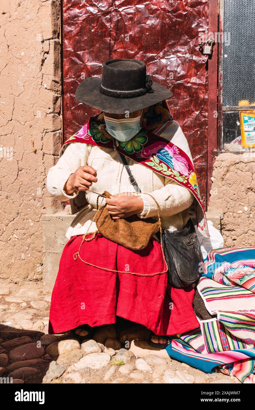 Arme indigene erwachsene Frau Handwerkerin mit blauer Maske und typischer Ahnenweberei in Zeiten der covid-19-Pandemie an einem sonnigen Tag im Andes mou Stockfoto