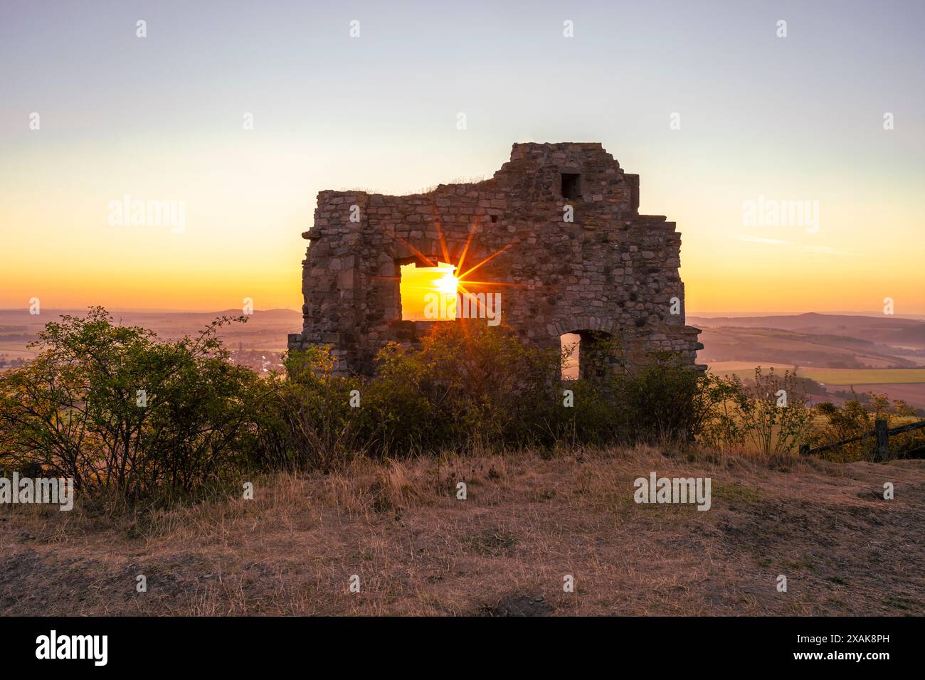 Mauern der Burgruine Desenberg in der Warburger Börde scheint die aufgehende Sonne durch die Öffnung in der Mauer und bildet einen Sonnenstern. Warburg, Landkreis Höxter, Nordrhein-Westfalen, Deutschland Stockfoto