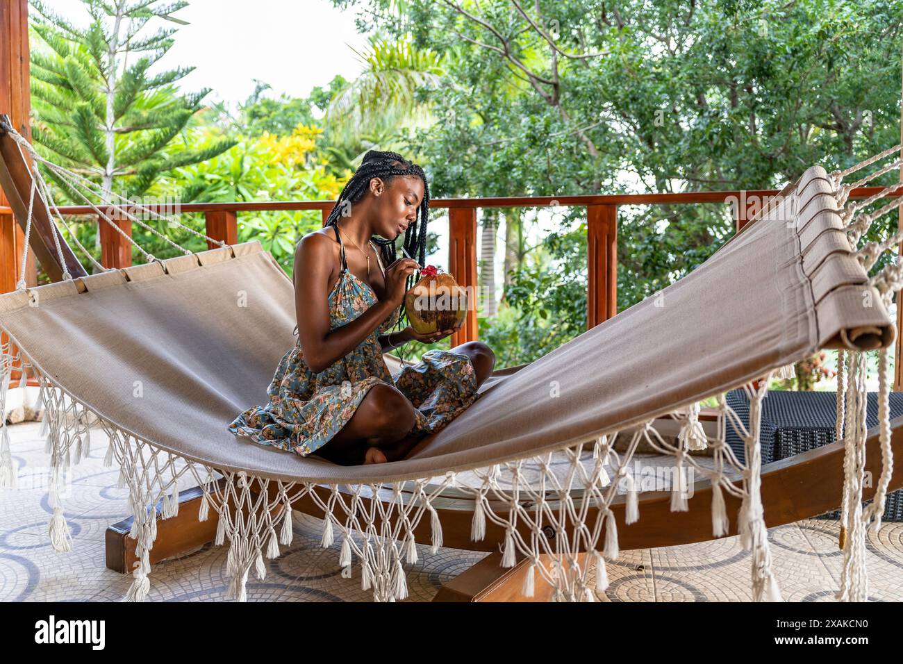 Nordamerika, Karibik, Hispaniola Island, Dominikanische Republik, Samana-Halbinsel, Sanchez, Jardines La Loma, ziemlich dunkelhäutige Latina sitzt in einer Hängematte und trinkt aus einer Kokosnuss Stockfoto