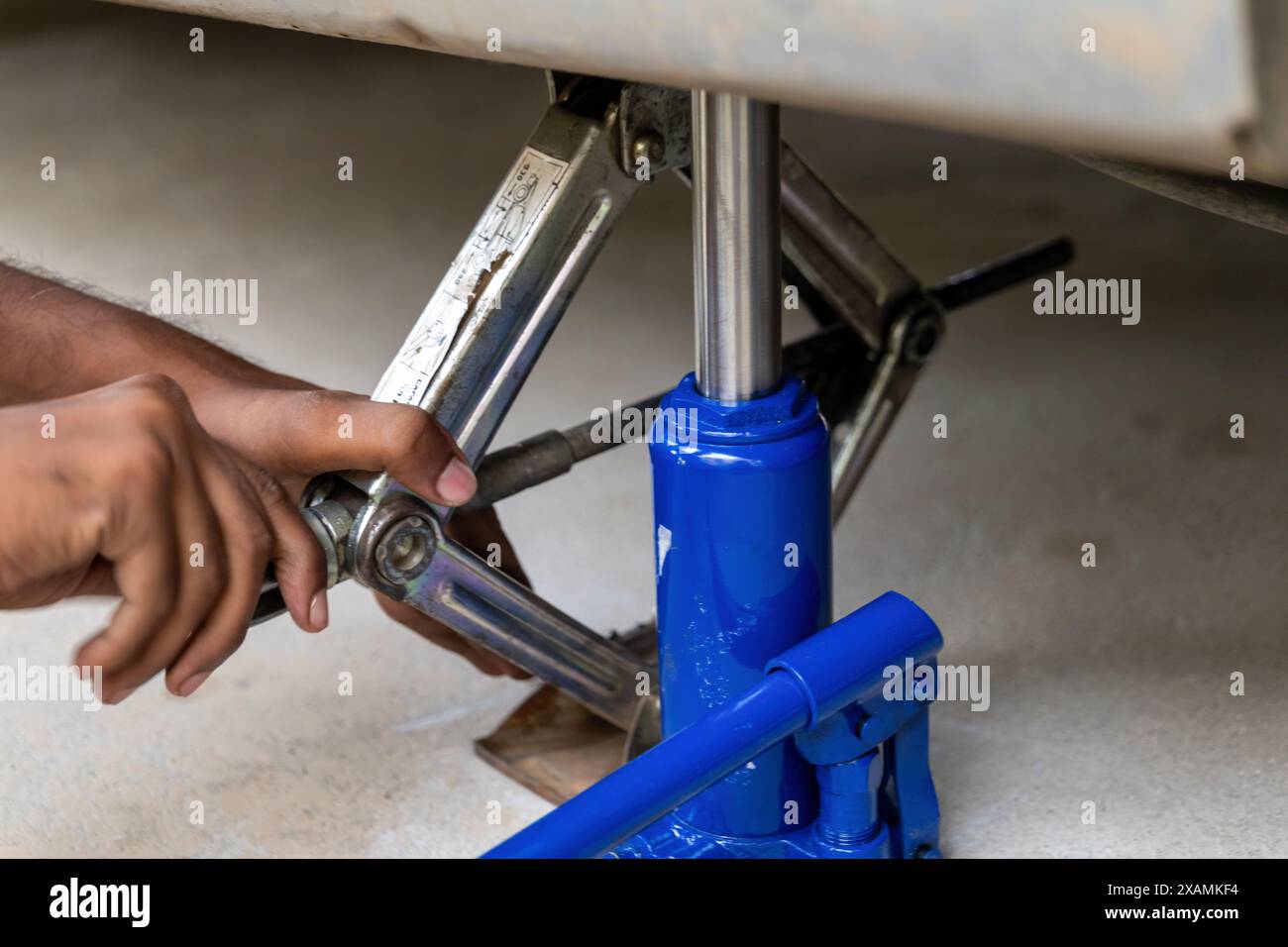Bei dieser Nahaufnahme bedient ein Paar Hände fachmännisch einen Flaschenheber und einen Scherenheber, um ein Fahrzeug zur Wartung anzuheben. Diese robusten Werkzeuge spielen einen Cru Stockfoto