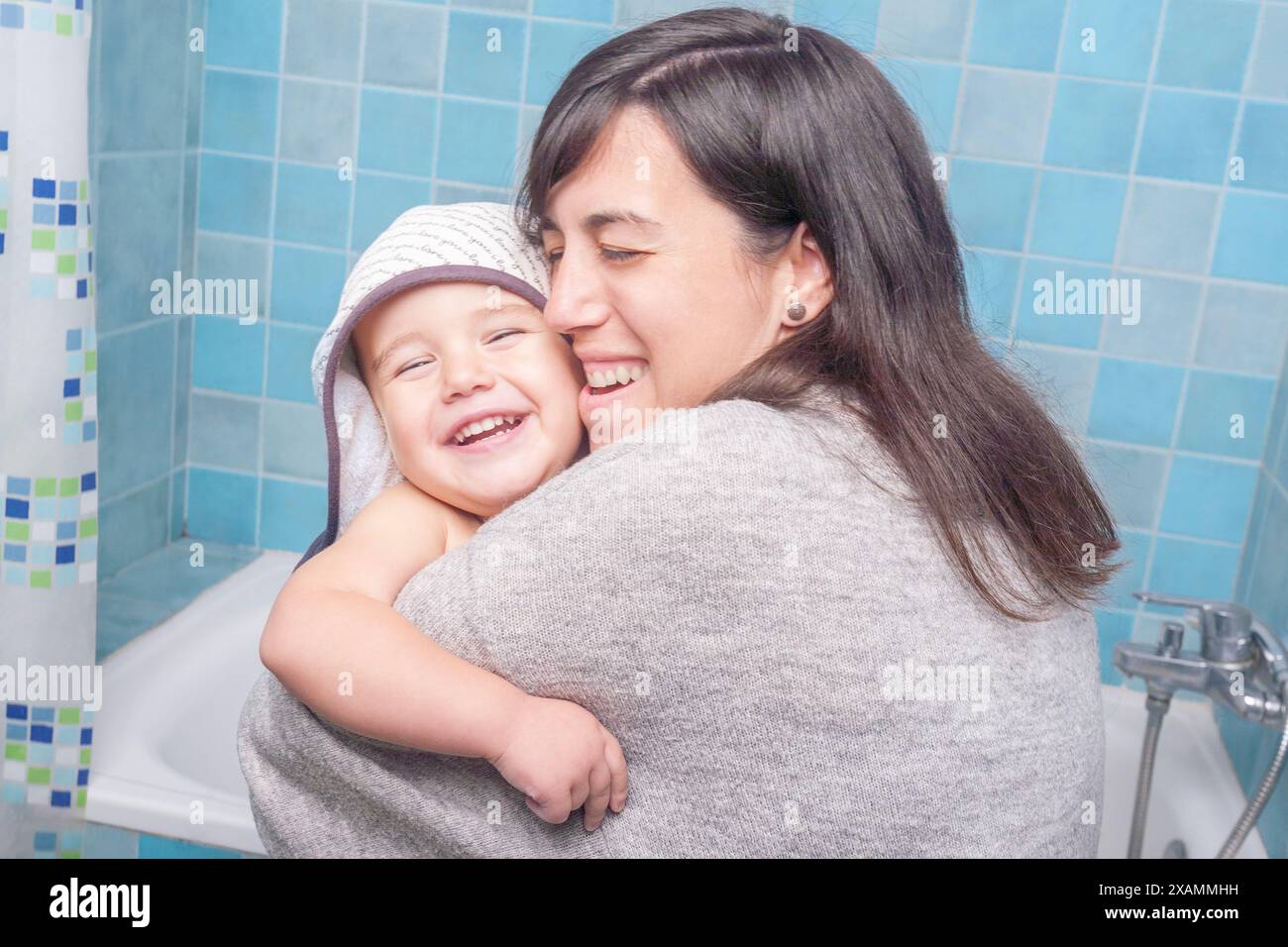 Eine Frau umarmt ein lächelndes Kind im Badezimmer und teilt einen warmen und liebevollen Moment. Stockfoto