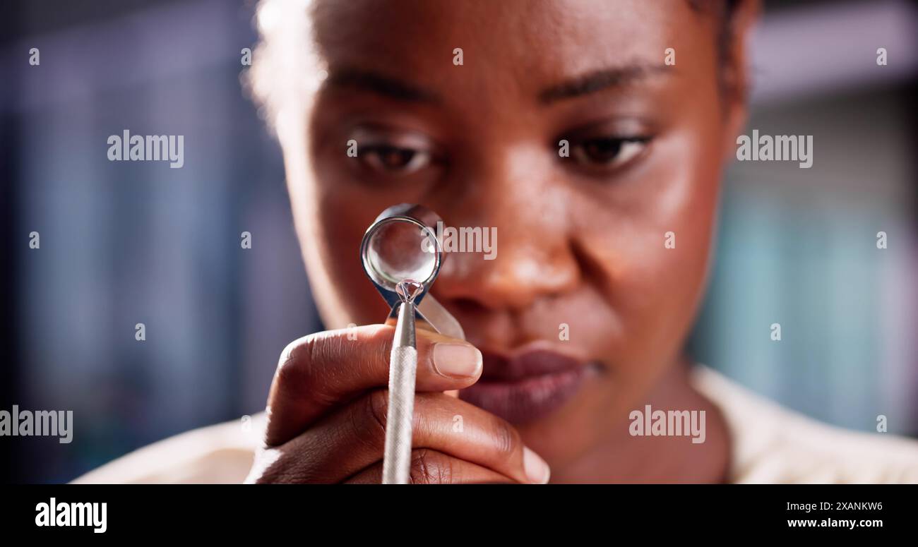 Afroamerikanische Juwelierin prüft Diamantqualität mit Lupe in der Schmuckwerkstatt für Werteinschätzung. Stockfoto