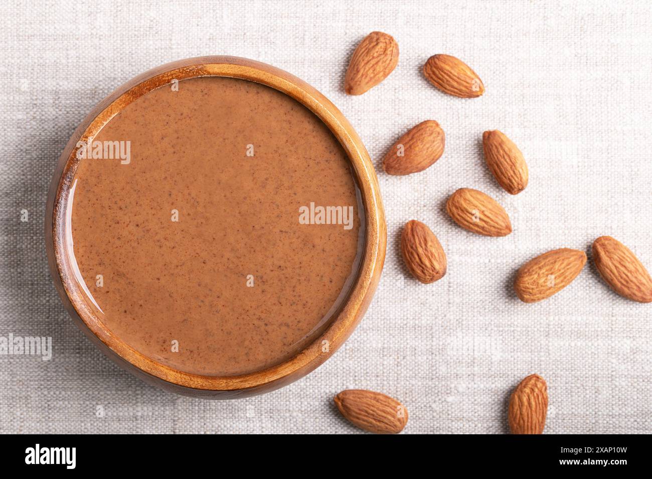 Braune Mandelbutter in einer Holzschale auf Leinengewebe. Glatte Lebensmittelpaste aus dem Mahlen von Mandeln zu Nussbutter. Prunus dulcis-Nüsse. Stockfoto