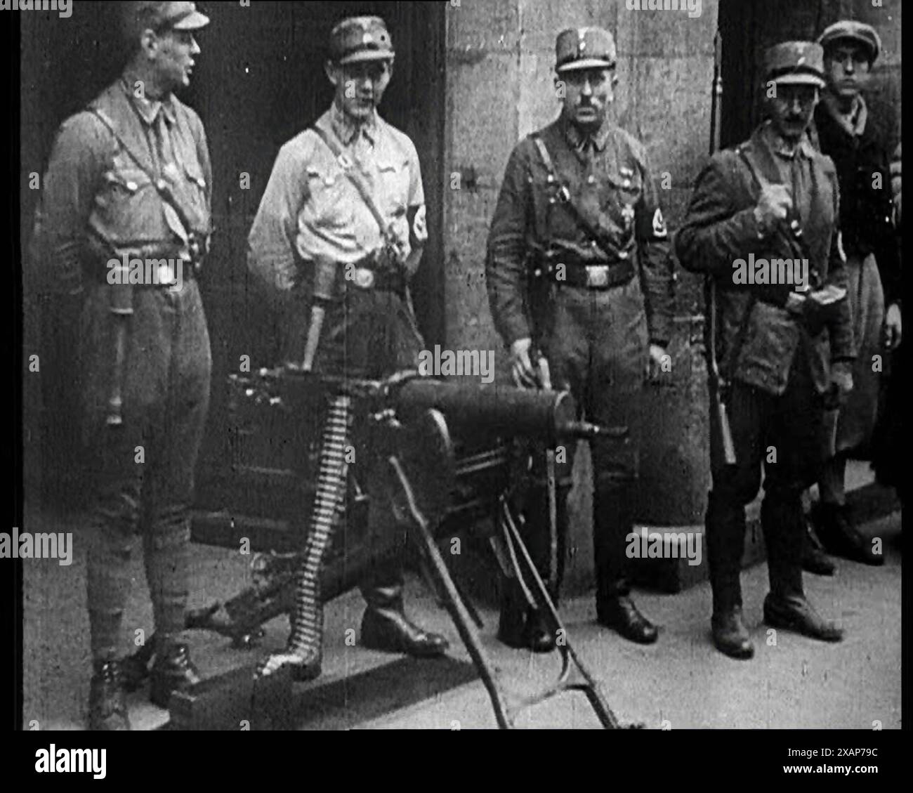 Uniformierte Nazis stehen neben einem Maschinengewehr, 1933. Der Aufstieg des Nationalsozialismus in Deutschland. Obwohl sie keine überwältigende Mehrheit erhielten, ließen die Nazis es so aussehen, als hätten sie es getan. Mit ihren neuartigen Techniken, ihrer Anziehungskraft und ihren lebendigen Methoden bestand kein Zweifel daran, dass sie in der Lage waren, die erforderliche Unterstützung zu erhalten." Aus „Time to Remember – The Time of the Monster“, 1933 (Reel 2); Dokumentarfilm über die Ereignisse von 1933, Rise of Roosevelt and Hitler. Stockfoto