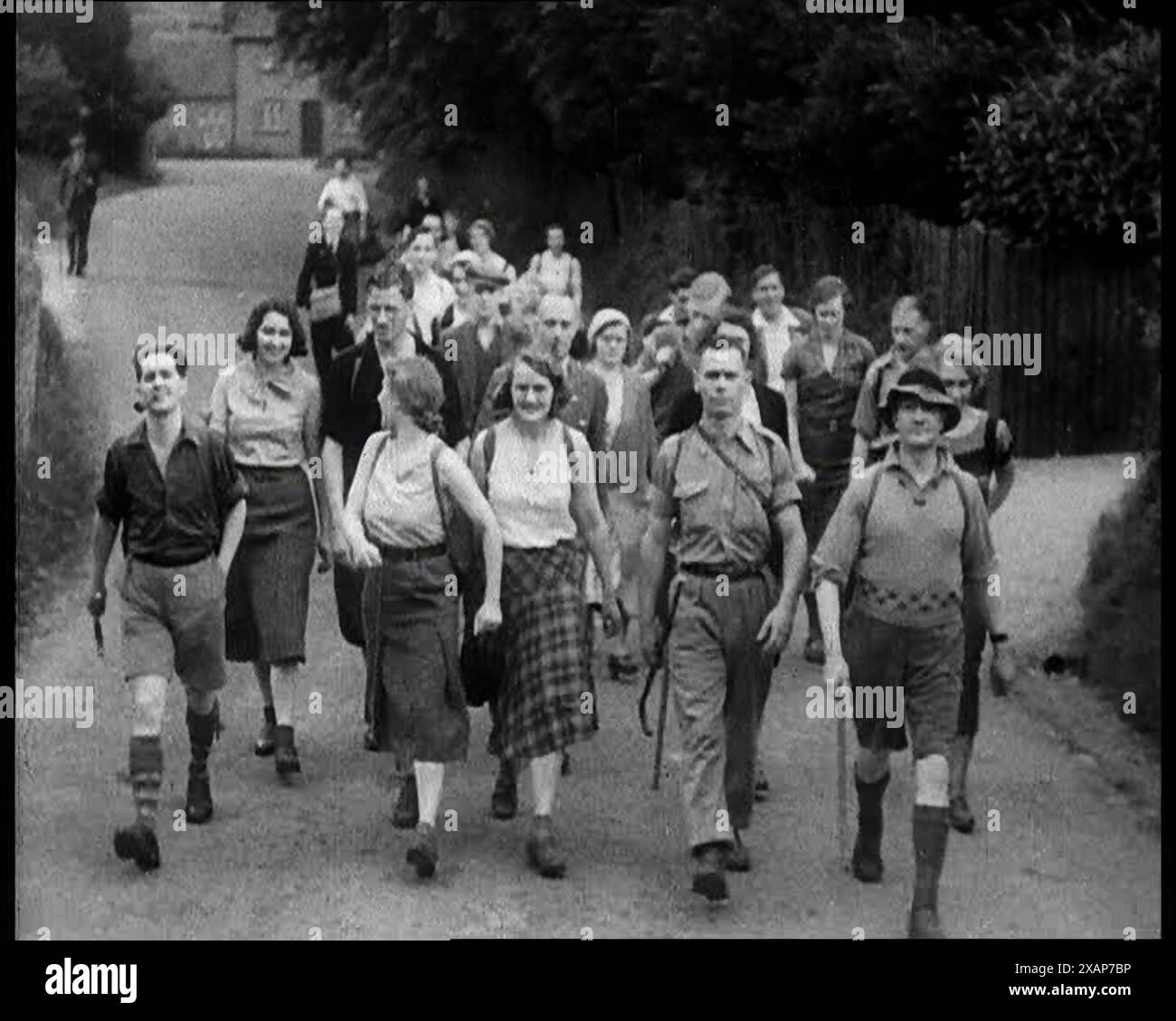 Leute, die eine Straße zur Kamera hinunterwandern, 1933. Es war [in diesem hellen Sommer], dass sie das Wandern erfanden. Es war, als bräuchte das Gehen nach einem Jahrhundert mechanischen Antriebs einen neuen Slogan, eine neue Spielerei, um es zu verkaufen... der Sommer der großen Wanderungen, der Sommer der Treffen in der freien Natur, der Sommer der Wiederentdeckung, in Shorts und Hemden. Der Massenüberfall von Kindern Scout war ein Protest beim Kinder Scout im Peak District, Derbyshire, der am 24. April 1932 stattfand. Der Protest sollte darauf hinweisen, dass Wanderern der Zugang zu Gebieten mit offenem Land verweigert wurde Stockfoto