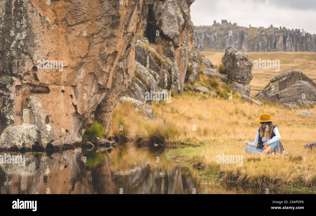 Eine Frau sitzt auf einem Feld neben einem Fluss, touristisch in den peruanischen anden, Huaillay, Pasco, Peru. Stockfoto