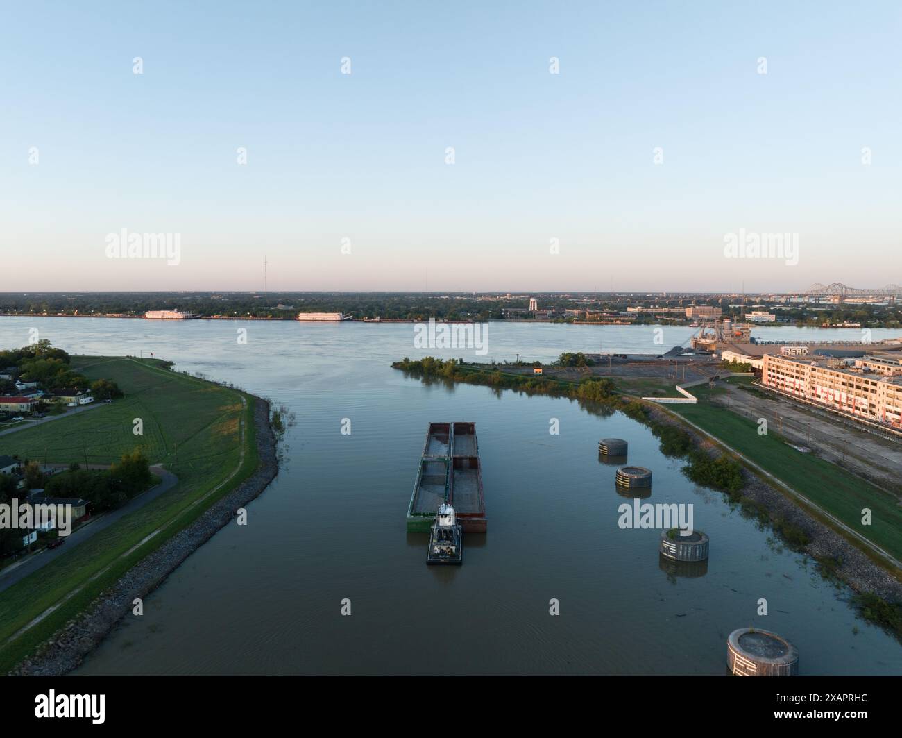 Aus der Vogelperspektive lässt ein Binnenschiff den Industriekanal in New Orleans' historischem 9th Ward verlassen und bei Sonnenaufgang in den Mississippi River eindringt. Stockfoto