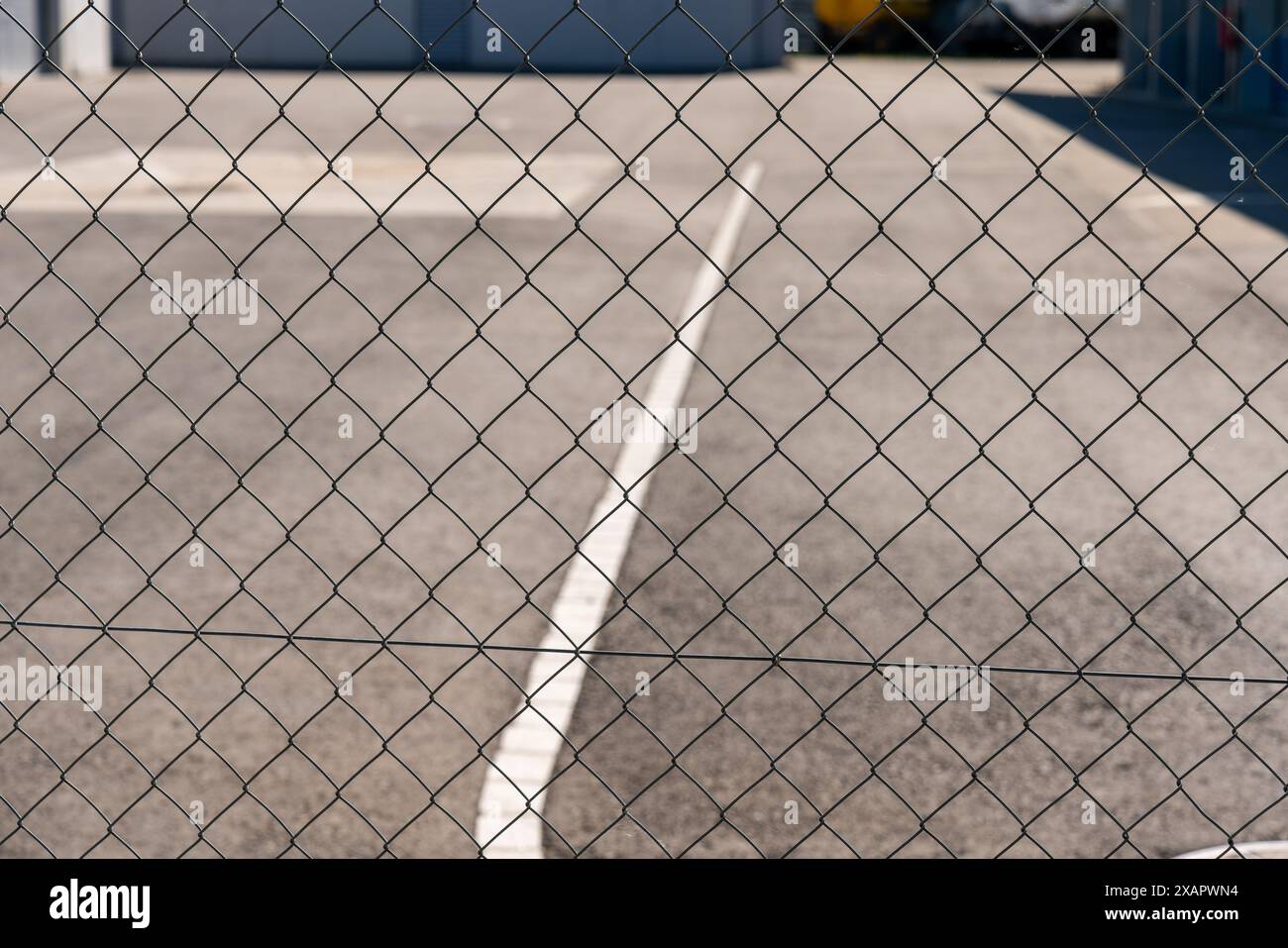 Maschendrahtzaun vor Asphaltroadd mit weißen Straßenmarkierungen. Stockfoto