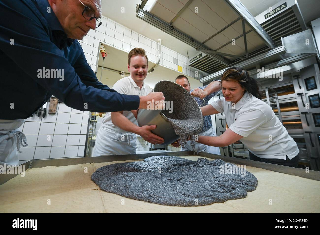 Allstedt, Deutschland. Juni 2024. Rüdiger Malter (l-r), Staatssekretär im Finanzministerium des Landes Sachsen-Anhalt, Vincent Richter von der Bäckerei Meye, Daniel Kirchner, Bürgermeister von Allstedt, und Bianca Richter gießen die Mohnmischung auf den weltweit größten Mohnkuchen. Der Rekordversuch ist eine Kampagne der Kunststiftung Sachsen-Anhalt zum Gedenkjahr „500 Jahre Bauernkrieg und 500. Todestag Thomas Müntzers“ im Jahr 2025. Müntzer hielt 1524 seine berühmte Predigt auf der Burg in Allstedt. Quelle: Heiko Rebsch/dpa/Alamy Live News Stockfoto