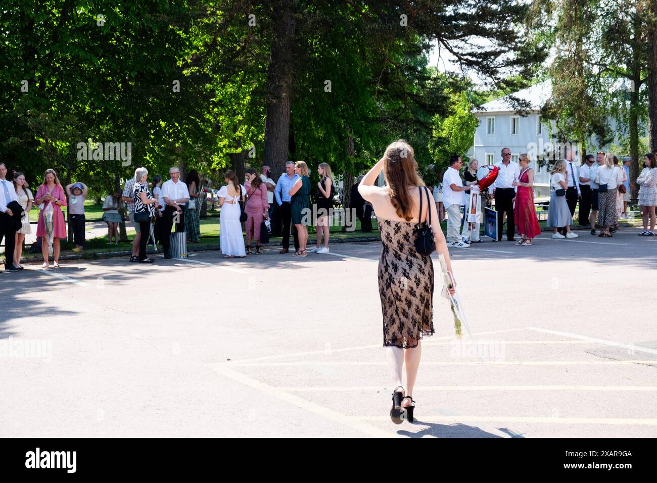 FRAU TRÄGT ROSE IN SOMMERKLEID, Åland, FINNLAND: Familien versammeln sich vor dem Schulgebäude vor dem Schulabschluss 2024 im Åland Åland Lyceum (Ålands Gymnasium) in Mariehamn, Åland Archipel, Ostsee, Finnland – an diesem Tag verlassen die Schüler die Schule zum letzten Mal. Im Rahmen dieser nordischen Tradition werden Plakate mit Babybildern der Absolventen aufgeklebt und die Studenten selbst tragen ihre Studentmössa im Matrosenstil und kleiden sich in Anzügen (Jungen) und weißen Kleidern (Mädchen). Foto: Rob Watkins. Stockfoto