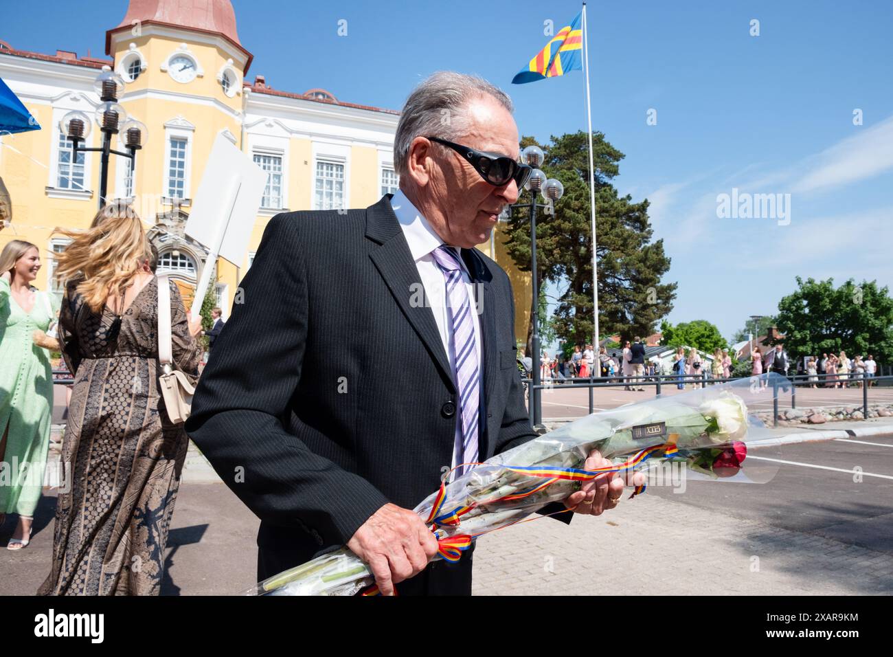 GROSSVATER, ROSEN BLUMEN, Åland: Ein stolzer Großvater mit Blumen, während Familien sich vor dem Hauptschulgebäude zum Åland-Abschlussfeiertag 2024 im Åland Lyceum (Ålands Gymnasium) in Mariehamn, Åland-Archipel, Ostsee, Finnland versammeln – an diesem Tag verlassen die Schüler die Schule zum letzten Mal. Im Rahmen dieser nordischen Tradition werden Plakate mit Babybildern der Absolventen aufgeklebt und die Studenten selbst tragen ihre Studentmössa im Matrosenstil und kleiden sich in Anzügen (Jungen) und weißen Kleidern (Mädchen). Foto: Rob Watkins. Stockfoto