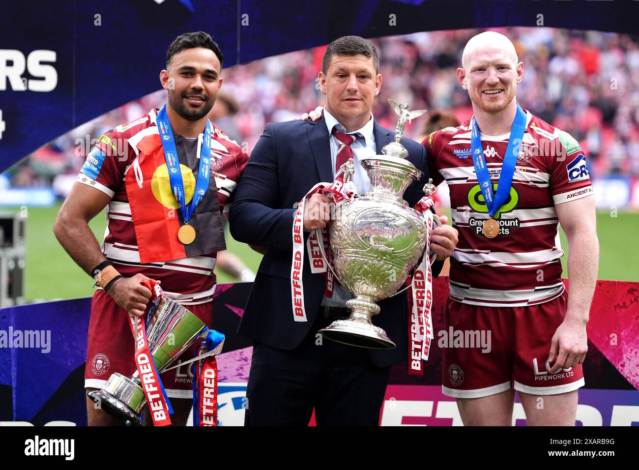 Matt Peet, Cheftrainer der Wigan Warriors (Mitte), posiert mit der Trophäe, Spieler Bevan French (links) mit der Trophäe „Mann des Matches“ und Liam Farrell feiern nach der letzten Pfeife im Finale des Betfred Challenge Cup im Wembley Stadium, London. Bilddatum: Samstag, 8. Juni 2024. Stockfoto