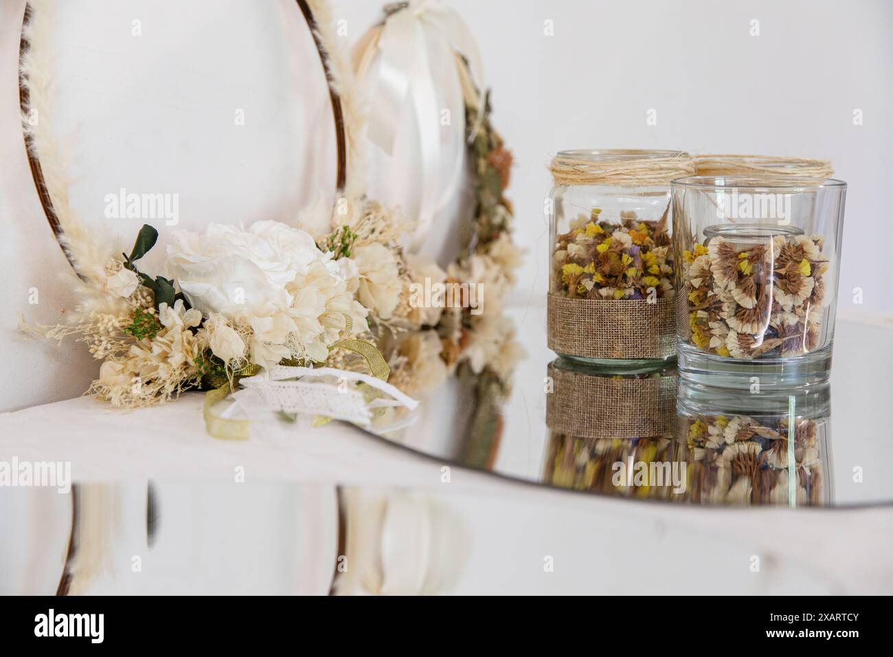 Zarte Blumenkränze mit weißen Rosen und getrockneten Blumen, begleitet von Gläsern mit getrockneten Blüten Stockfoto