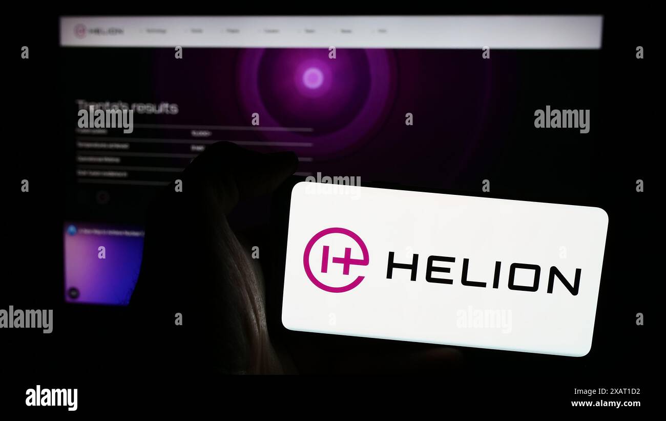 Person, die ein Mobiltelefon mit dem Logo des amerikanischen Fusionsenergieunternehmens Helion Energy Inc. Vor der Webseite des Unternehmens hält. Schwerpunkt auf dem Display des Telefons. Stockfoto