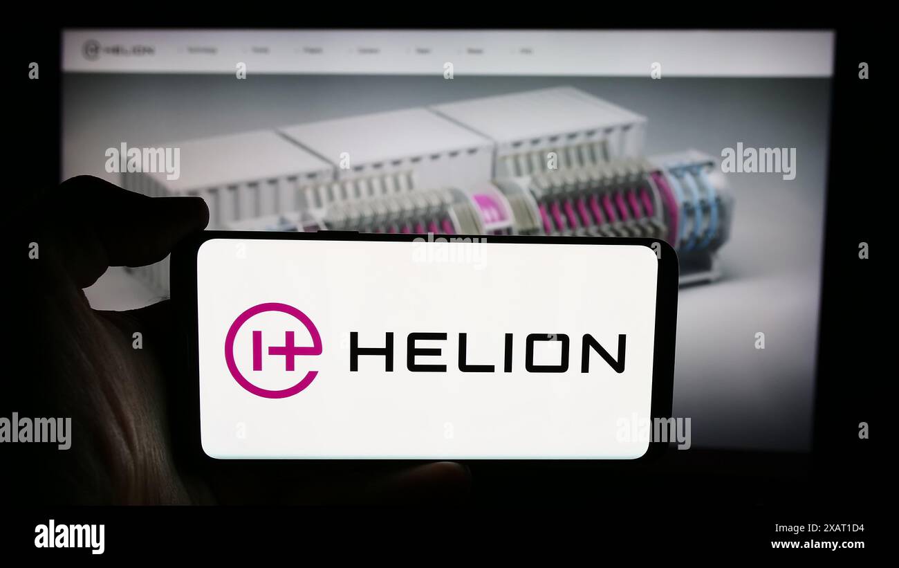 Person, die ein Mobiltelefon mit dem Logo des US-amerikanischen Fusionsenergieunternehmens Helion Energy Inc. Vor der Unternehmenswebseite hält. Schwerpunkt auf dem Display des Telefons. Stockfoto