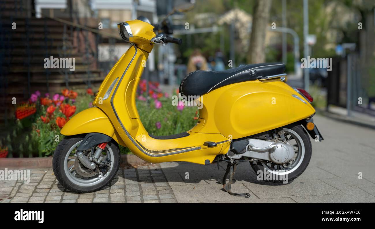 Motorroller Vintage gelb Farbe Motorrad geparkt auf gepflastertem Bürgersteig, verschwommener Stadthintergrund. Altmodisches Motorrad, Moped, Transportfahrzeug. Stockfoto