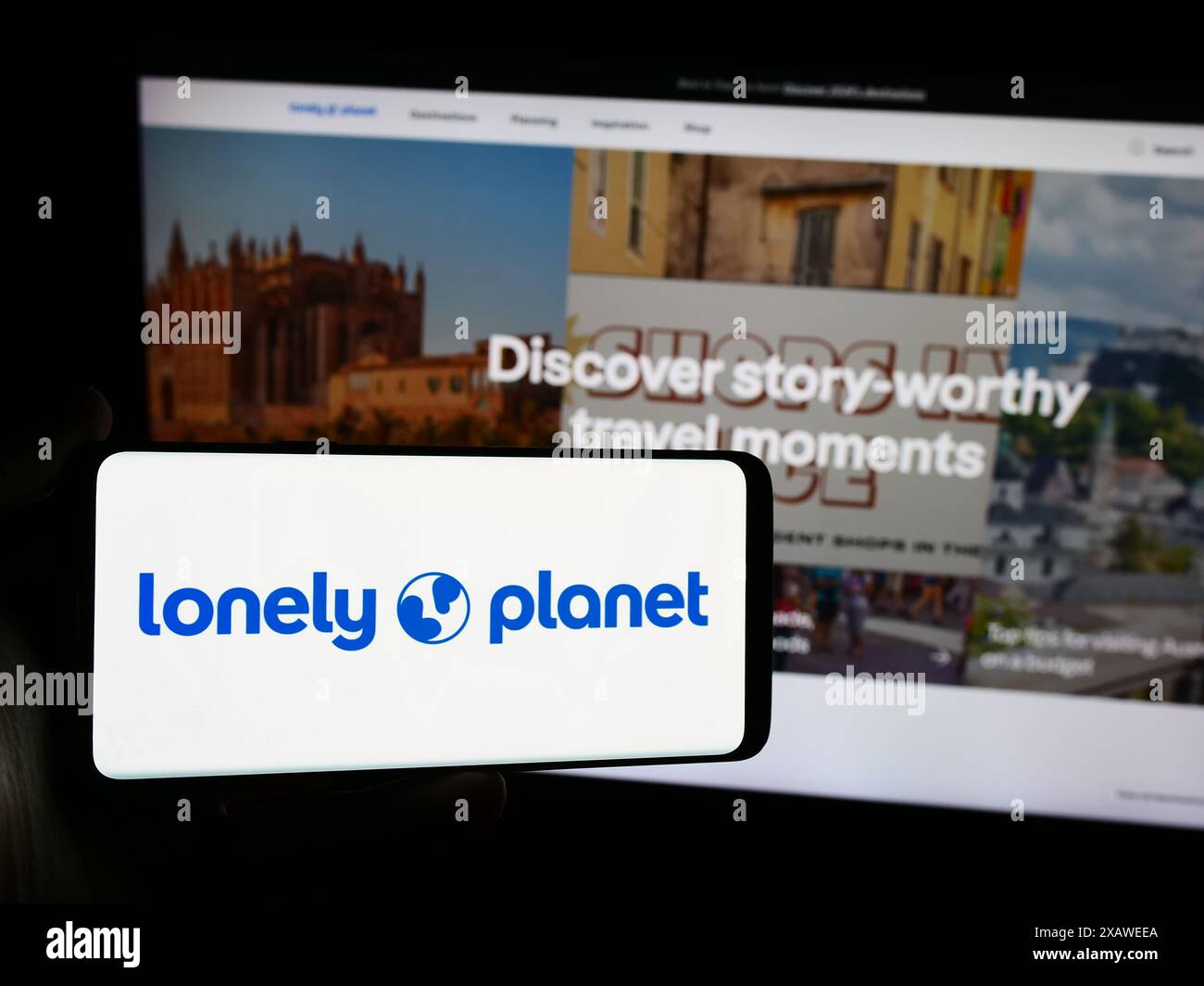 Person mit Smartphone und Logo des Reiseführers Lonely Planet vor der Website. Schwerpunkt auf dem Display des Telefons. Stockfoto