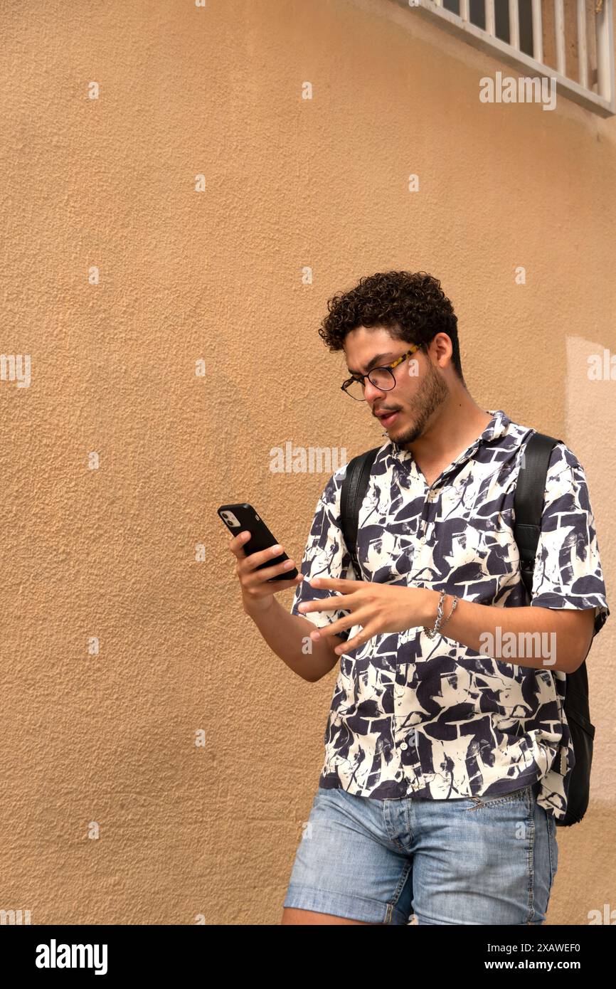 Moderner junger Mann mit Brille und Smartphone, der beim Gehen spricht. Technologie, Kommunikation, urbane Mode, aktiver Lebensstil Stockfoto