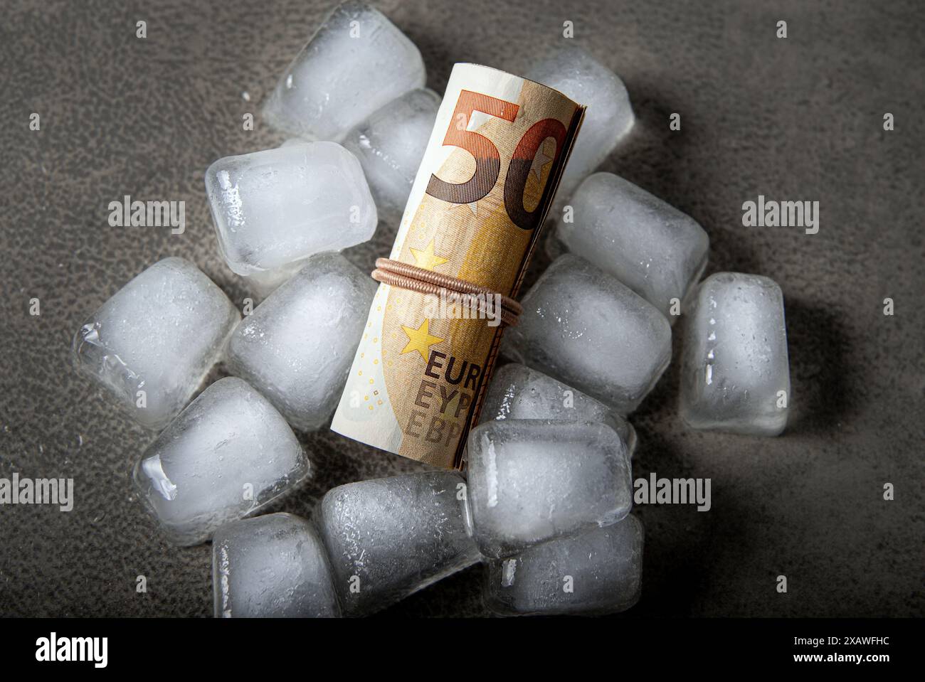 Konzept des Einfrierens der Gelder. Über dem Bild der Euro-Geldrolle in Eiswürfeln auf grauem Studiohintergrund. Kopierbereich. Stockfoto