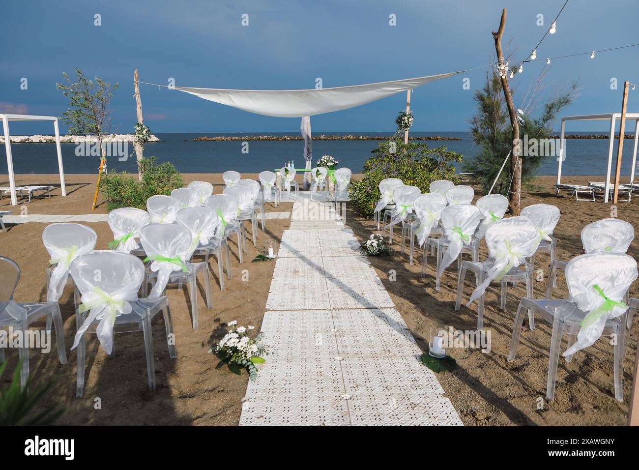 Elegante weiße Hochzeitsstühle werden an einem Sandstrand für eine Hochzeitszeremonie aufgestellt Stockfoto