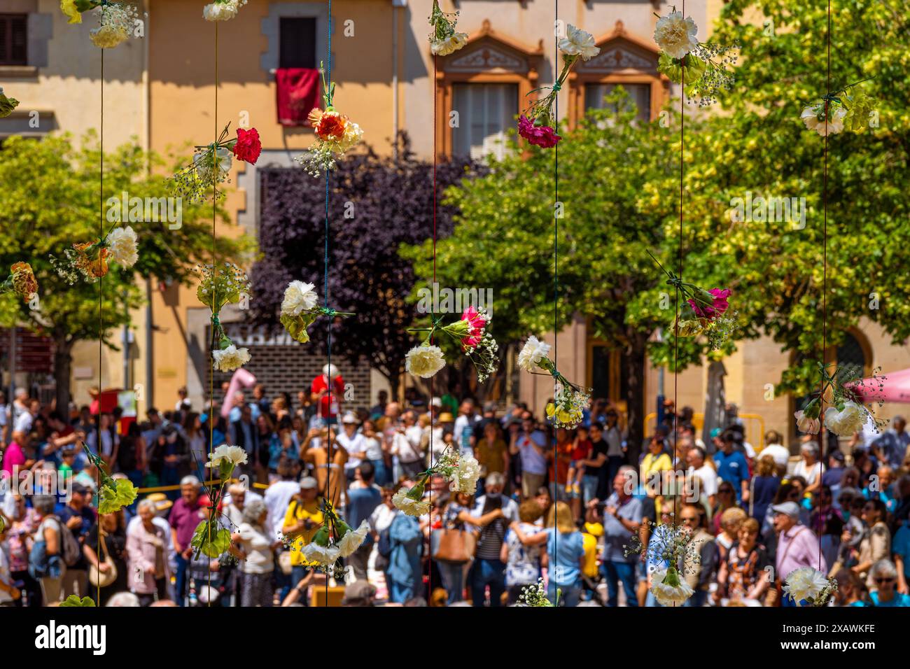 Farbenfrohe Blumen, die vertikal von grünen Fäden hängen, um das Blumenkorpus von La Garriga mit Menschen in Gruppen und Familien zu feiern Stockfoto