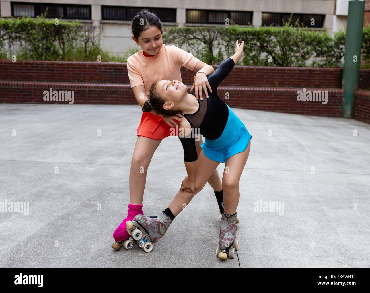 Zwei junge Mädchen in bunten Outfits üben gemeinsam im Park eine Skatingpose, lächeln und genießen ihre Zeit auf Rollschuhen. Stockfoto