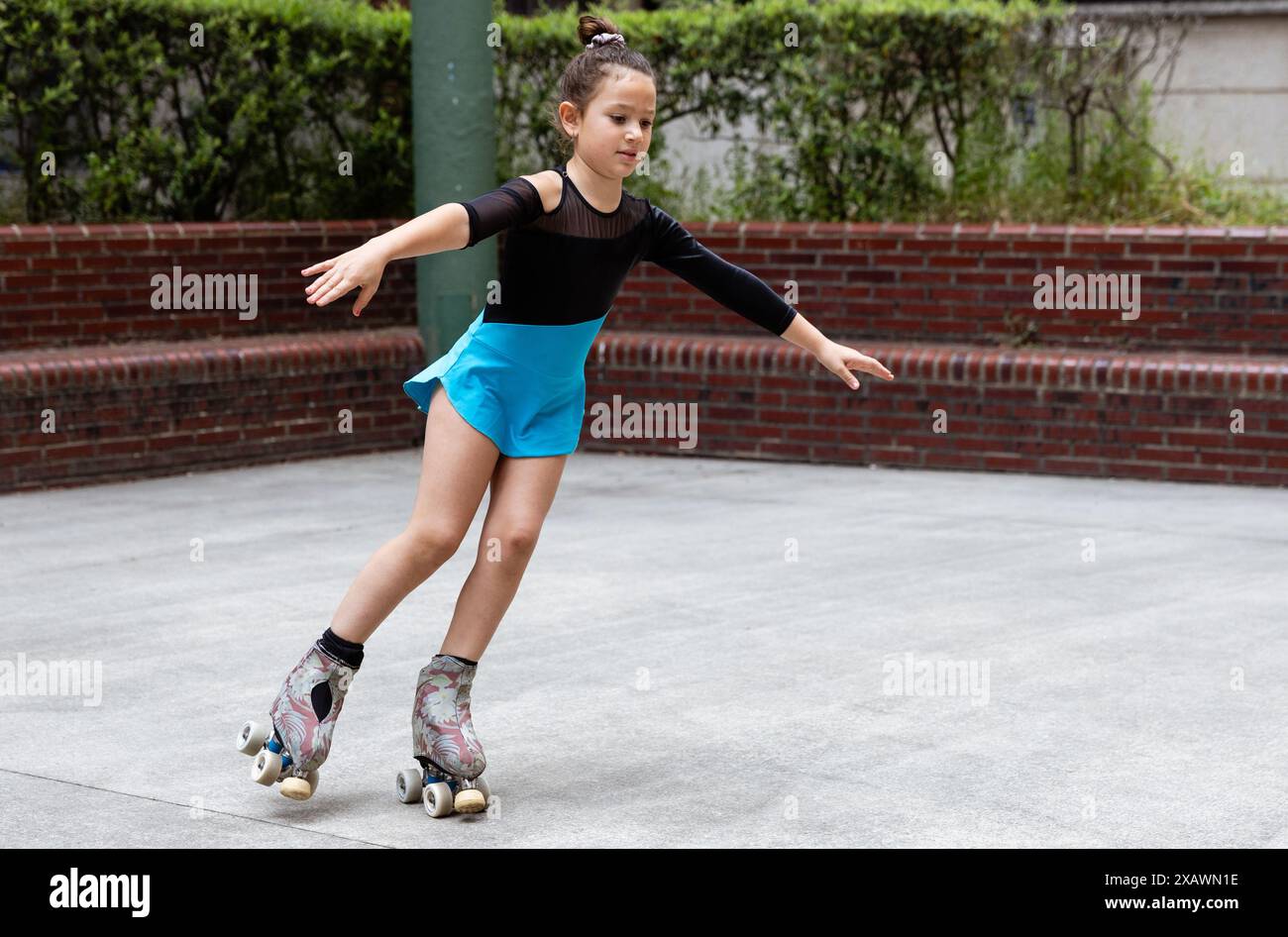 Ein junges Mädchen in blauem Rock und schwarzem Top Rollschuh läuft draußen auf glattem Untergrund und übt ihre Balance und Skating-Fähigkeiten aus. Stockfoto