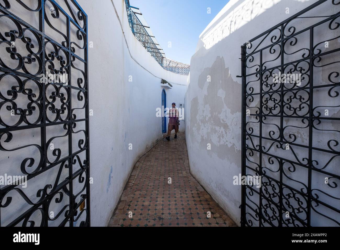 Ein Kellner bringt ein Tablett mit typisch marokkanischem Tee durch eine enge weiße Gasse und offene schmiedeeiserne Türen in Rabat, der Hauptstadt Marokkos in Nord-AF Stockfoto