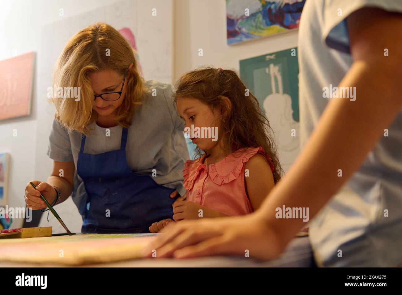 Kinder haben Kunstunterricht, Zeichnen, Malen mit dem Lehrer in der Werkstatt. Das Bild erfasst die unterstützende Interaktion zwischen Lehrer und Kind in einer kreativen und lehrreichen Atmosphäre Stockfoto