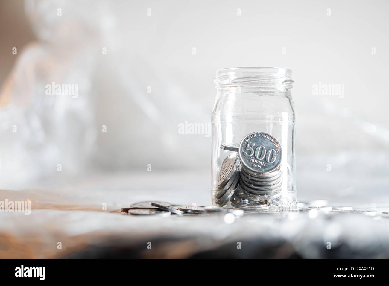 Ein Glasgefäß gefüllt mit 500 koreanischen Won-Münzen, platziert auf einer reflektierenden Oberfläche mit verschwommenem Hintergrund. Stockfoto