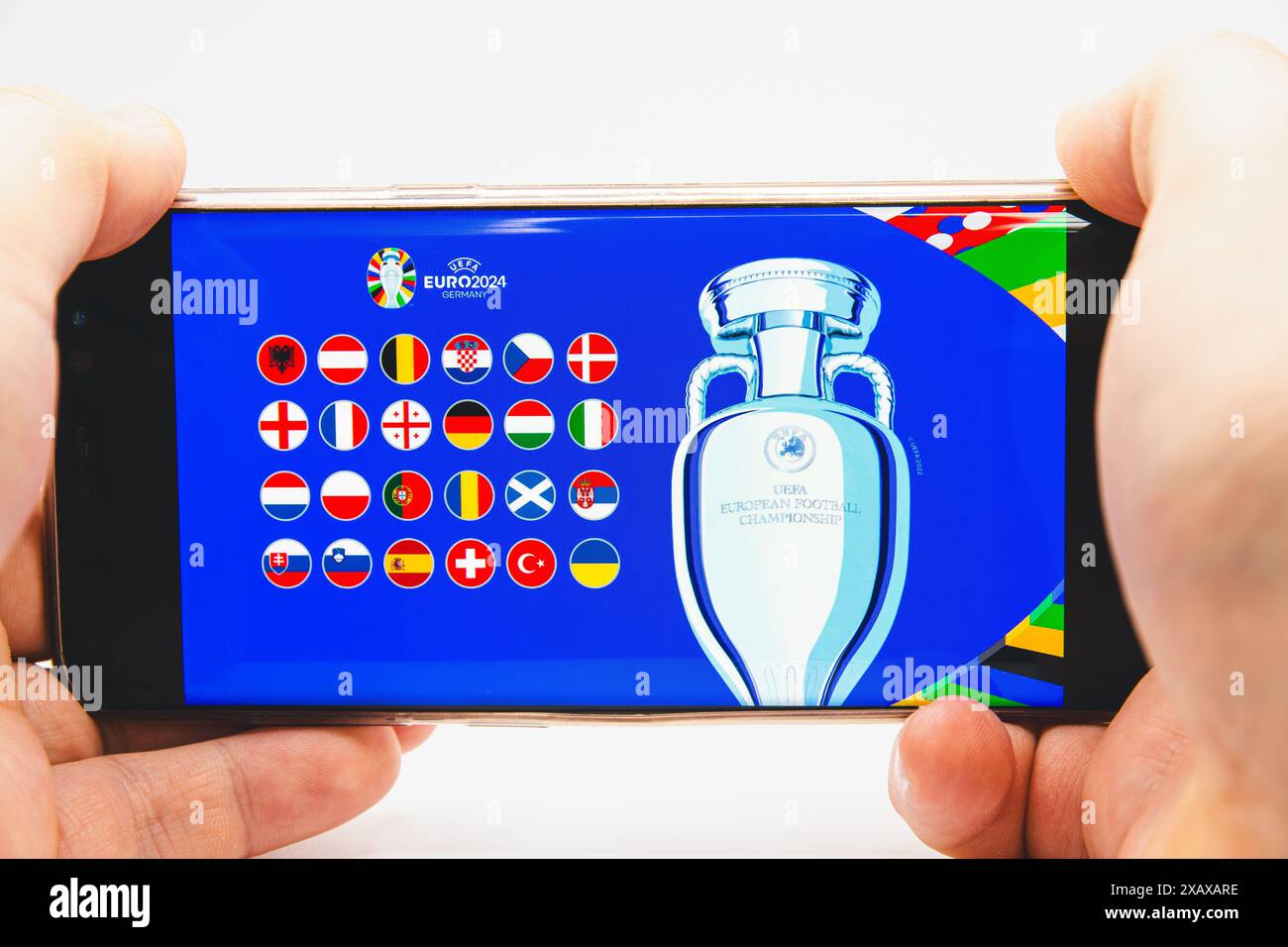 Ein Mann hält ein Smartphone mit dem offiziellen Logo der UEFA-Fußball-Europameisterschaft 2024 und Ikonen der Flaggen der teilnehmenden Länder Stockfoto