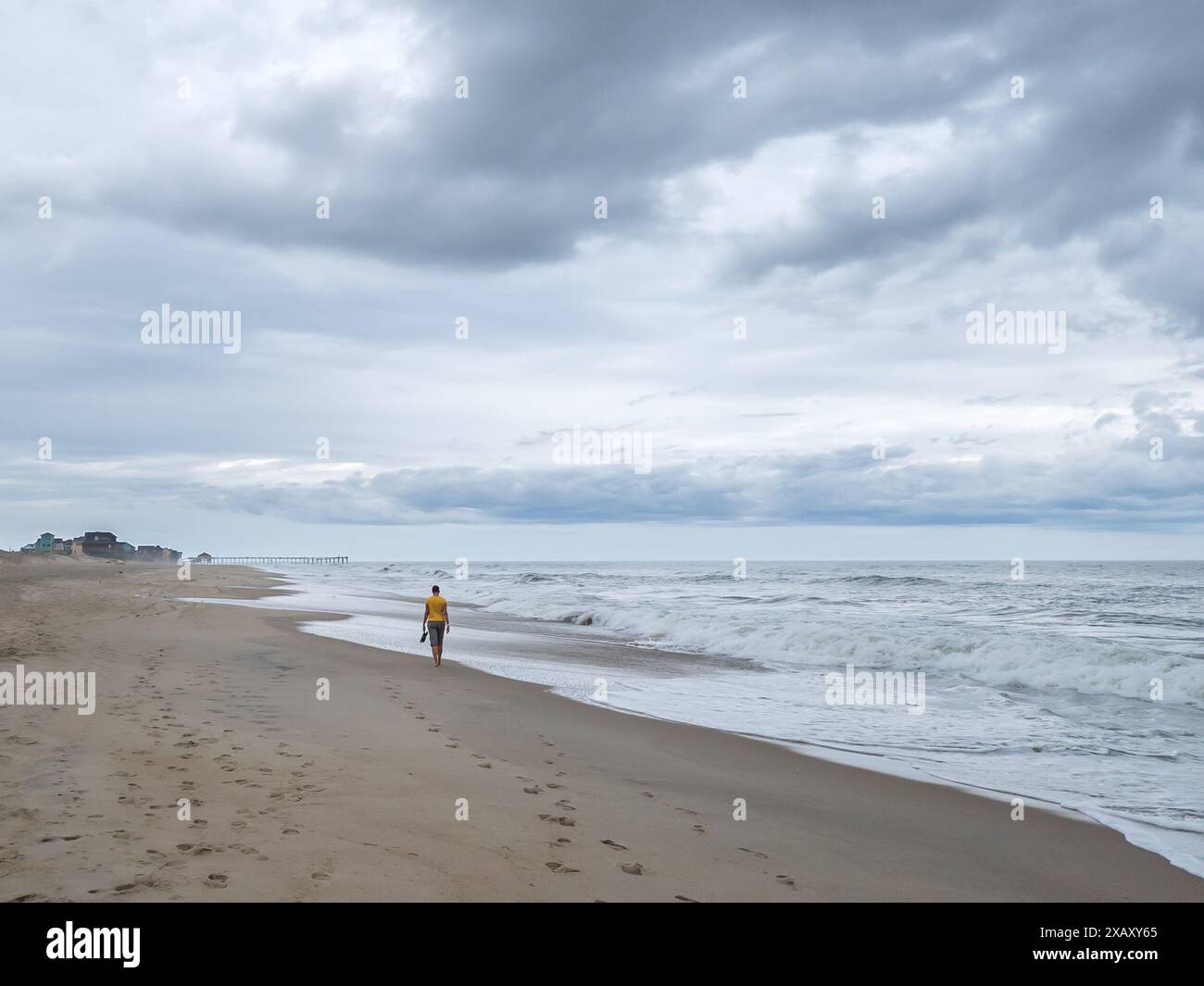 Eine Frau, die barfuß entlang der Atlantikküste in Richtung Rodanthe Pier am Cape Hatteras in North Carolina, USA, läuft Stockfoto